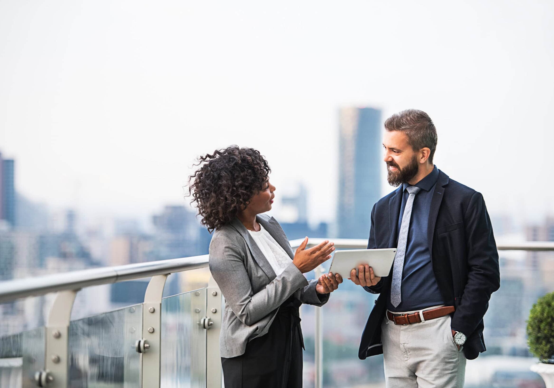 Professional Coach Conversations Two professional coaches having a discussion on a rooftop terrace, with a tablet in hand and a city skyline in the background.