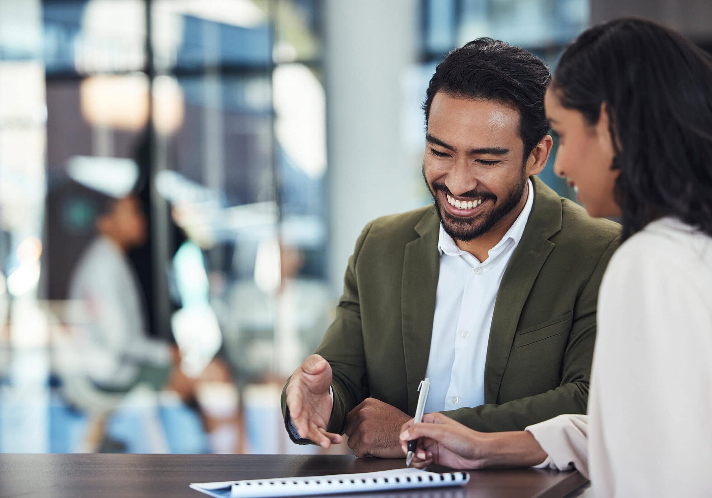 Coaching Partnerships A man in a suit jacket smiling and gesturing while speaking with a woman in a business setting, symbolizing coaching partnerships.